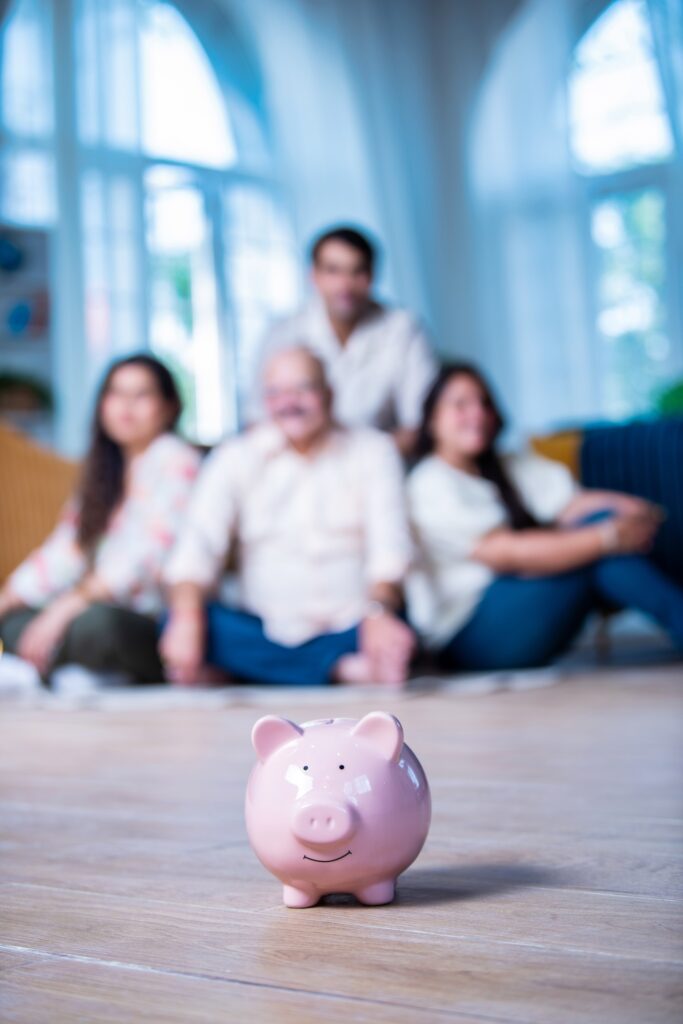 A smiling Indian family saves money with a piggy bank, looking at camera